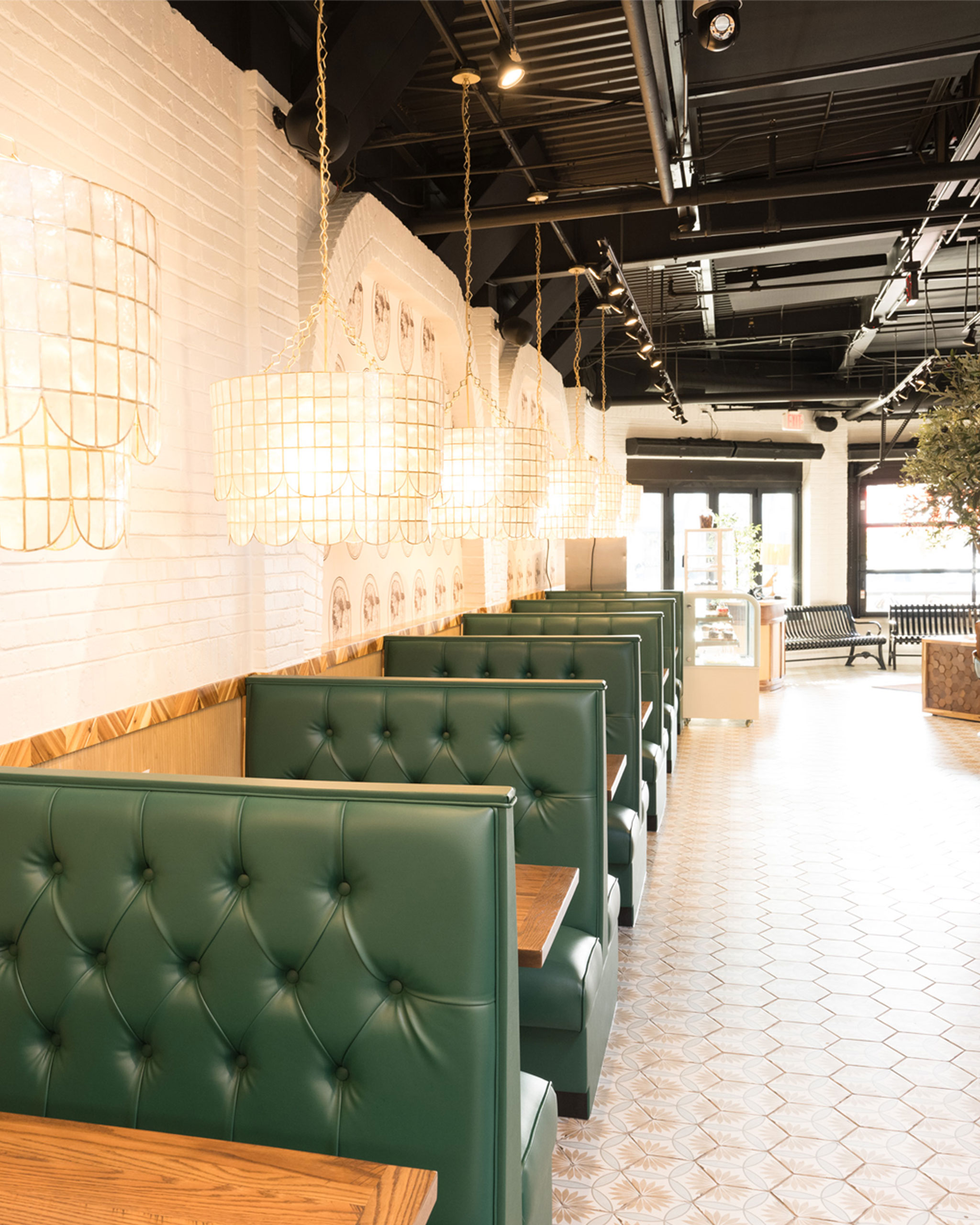 Elegant booth seating at The White Sheep café in Naperville with green tufted benches, pendant lights, and modern décor.