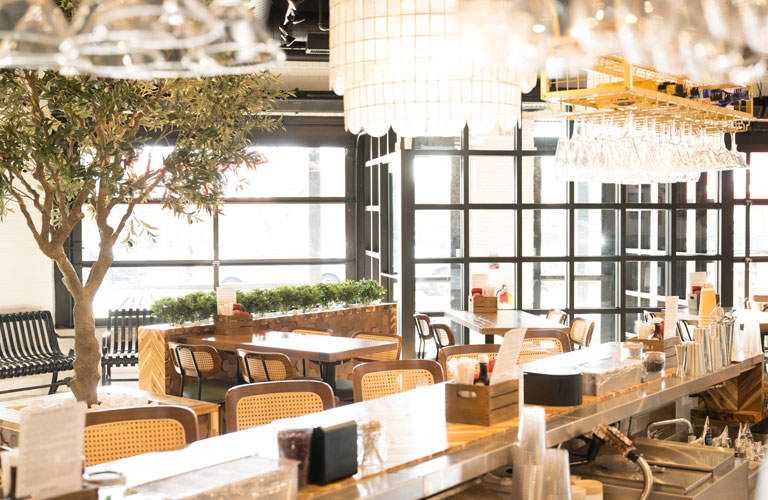 Event-ready seating at The White Sheep café in Naperville with bar counter, greenery, and natural light from floor-to-ceiling windows.