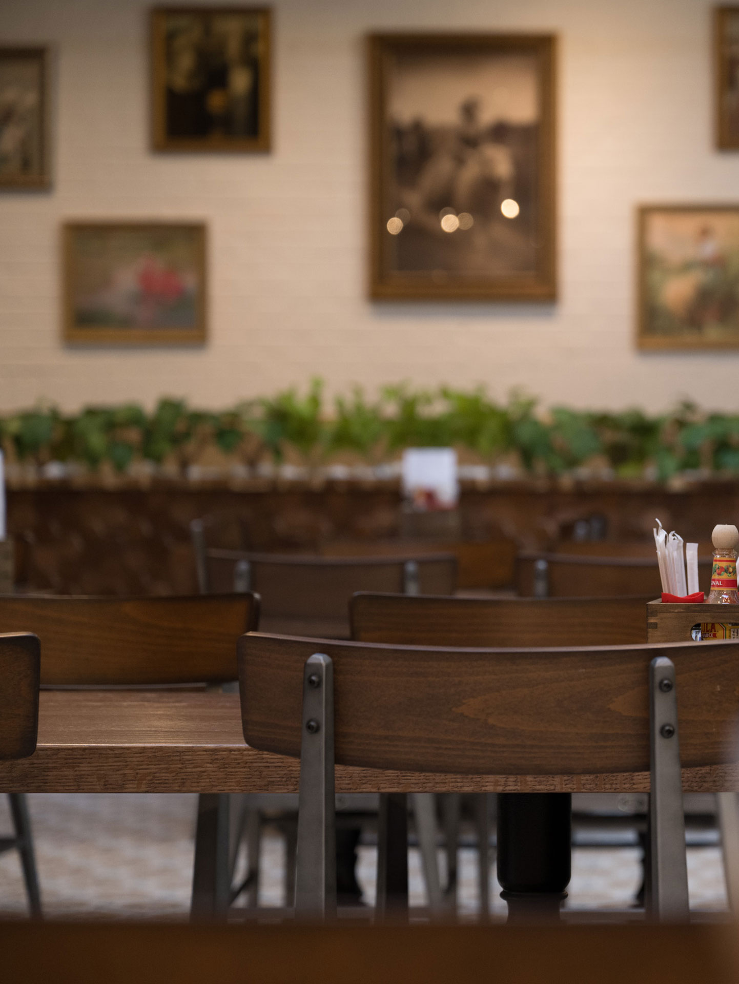 Close-up of dining tables at The White Sheep café in Naperville with wooden chairs, greenery, and framed wall art.